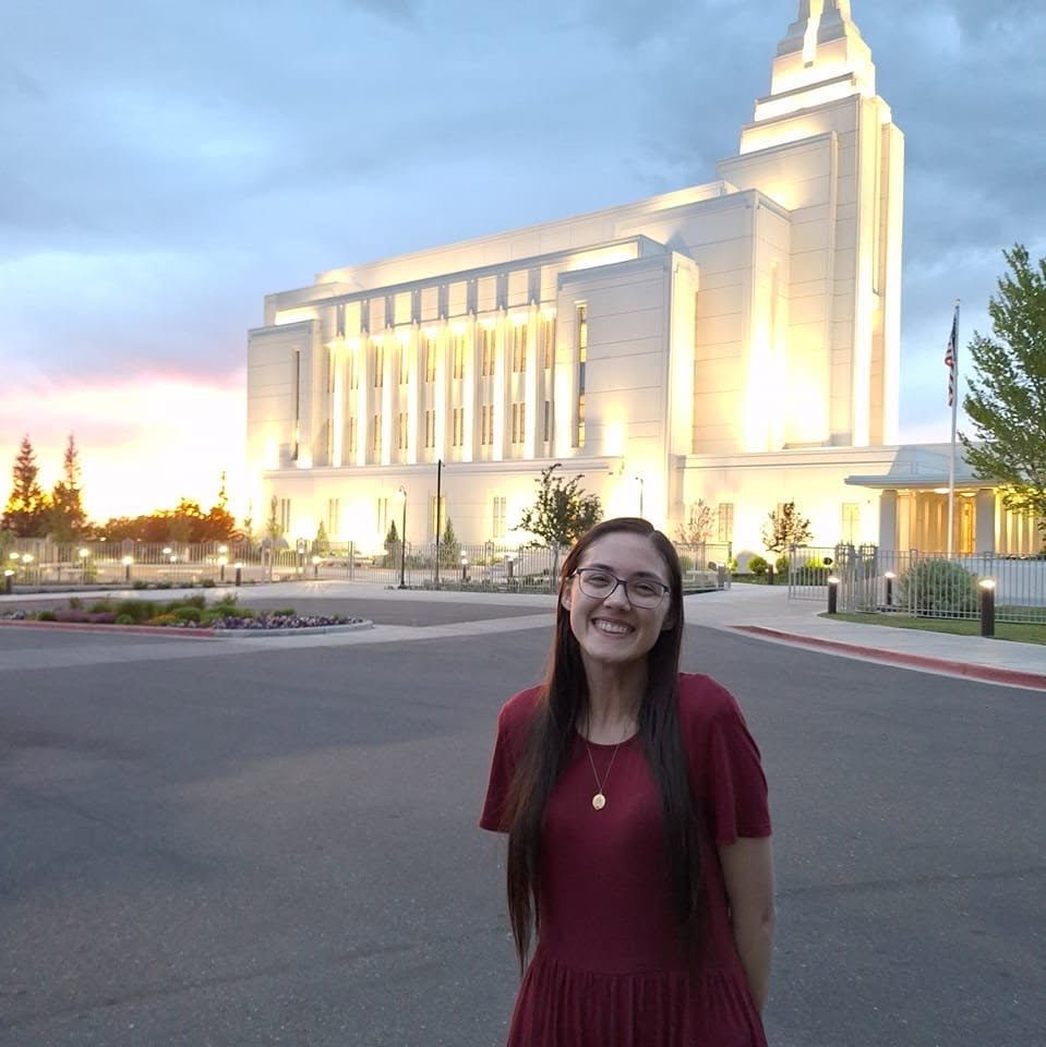 Rachel in a red dress standing in front of the Calgary Alberta Temple glowing at dusk