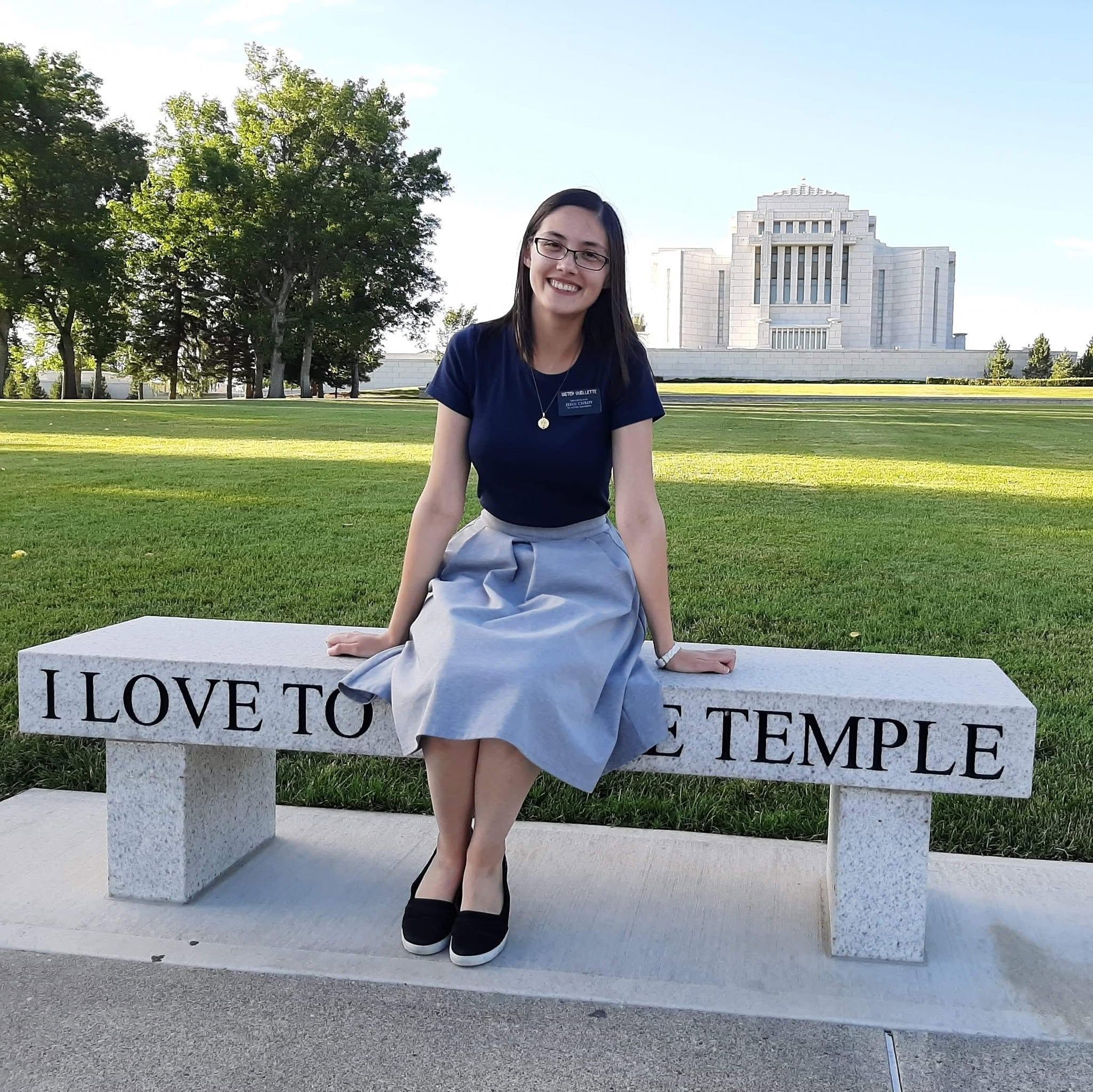 Rachel as a sister missionary sitting on a stone bench engraved "I love to see the temple", the Cardston Alberta Temple behind her