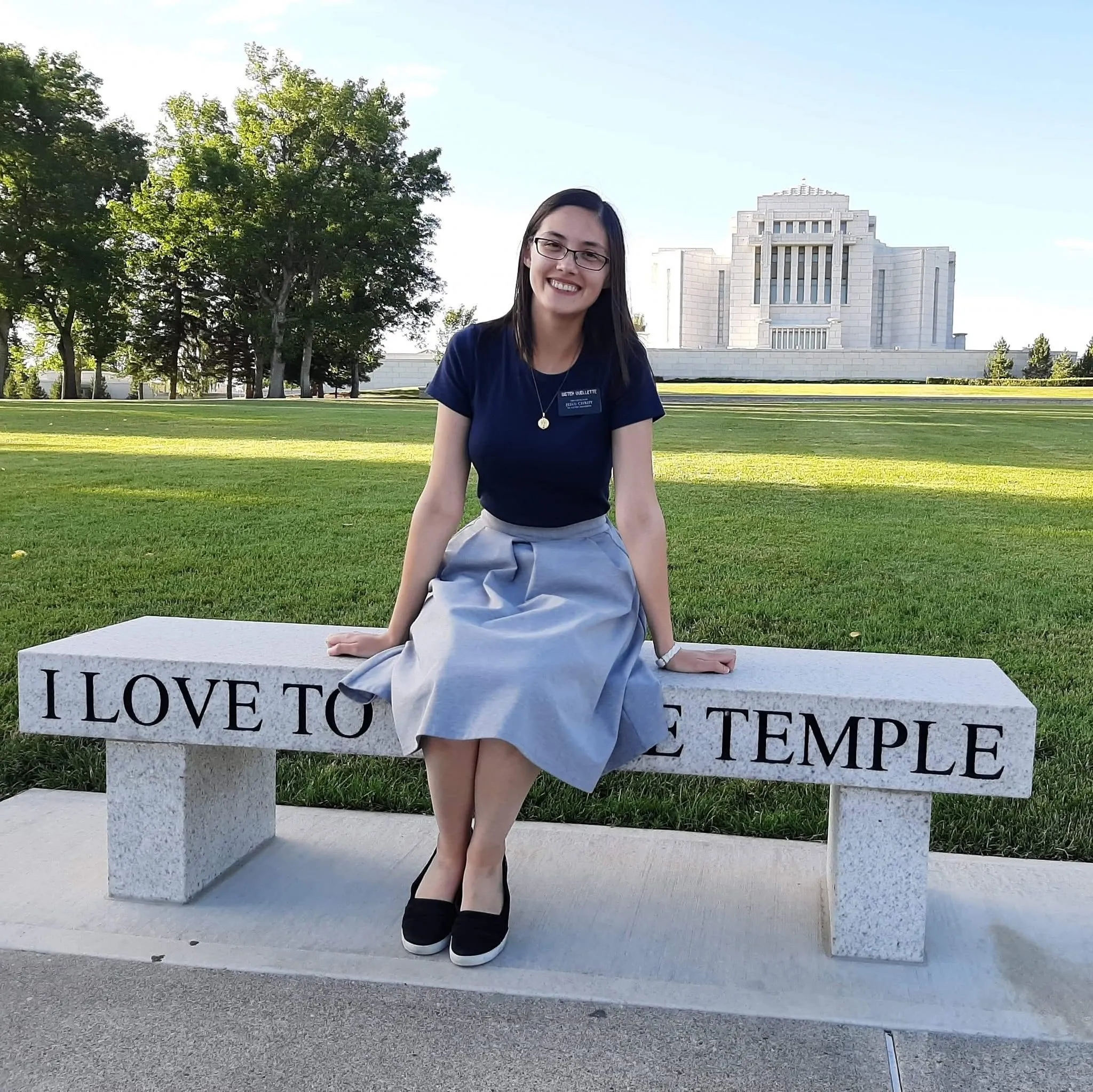 Rachel as a sister missionary sitting on a stone bench engraved "I love to see the temple", a white temple behind her