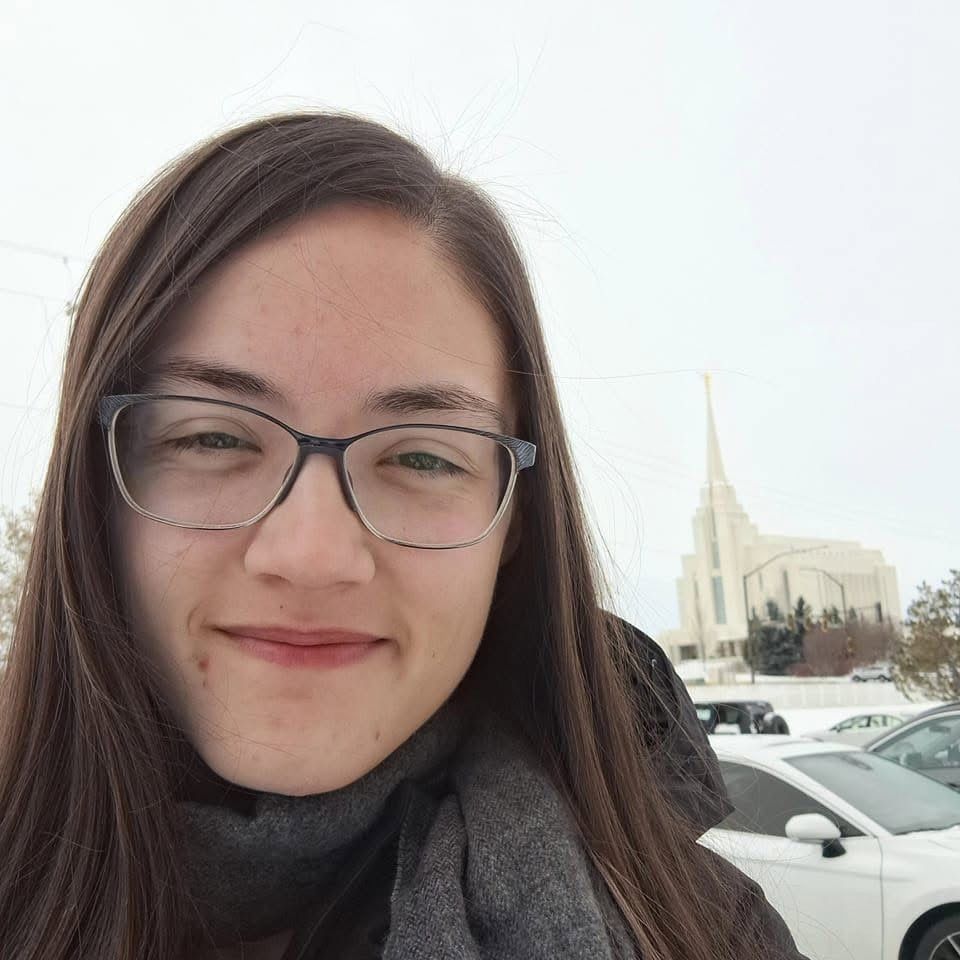 Close-up selfie of Rachel in a grey scarf on a wintry day, the Rexburg temple's spire behind her